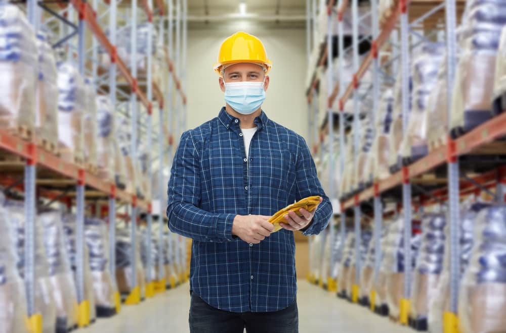 A man in a warehouse wearing PPE that includes a hard hat, mask, and gloves.