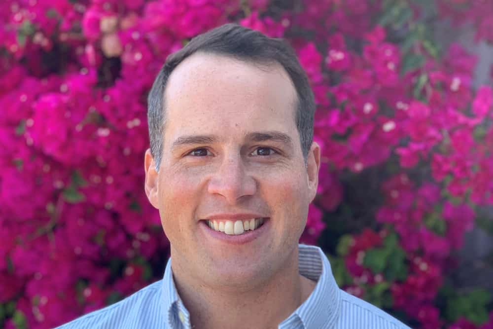 A man standing in front of a flower bush smiling