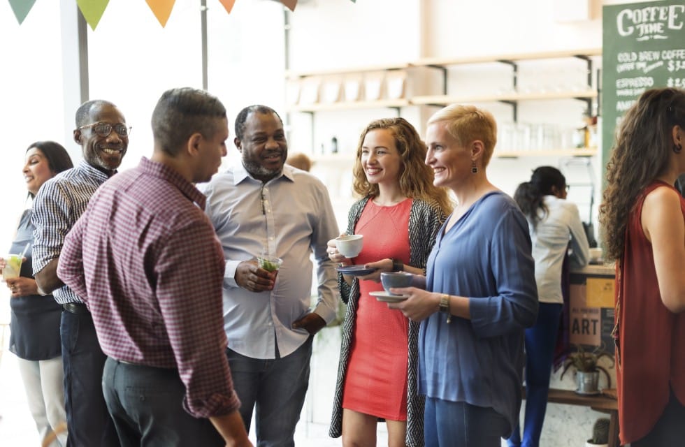 A group of people standing and talking while drinking coffee