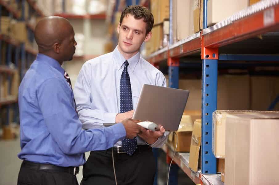 Two Warehouse Employees Work on a Laptop Inside of Warehouse