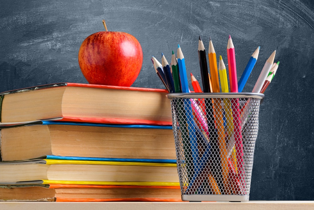 School books, with an apple on top and a container of colored pencils