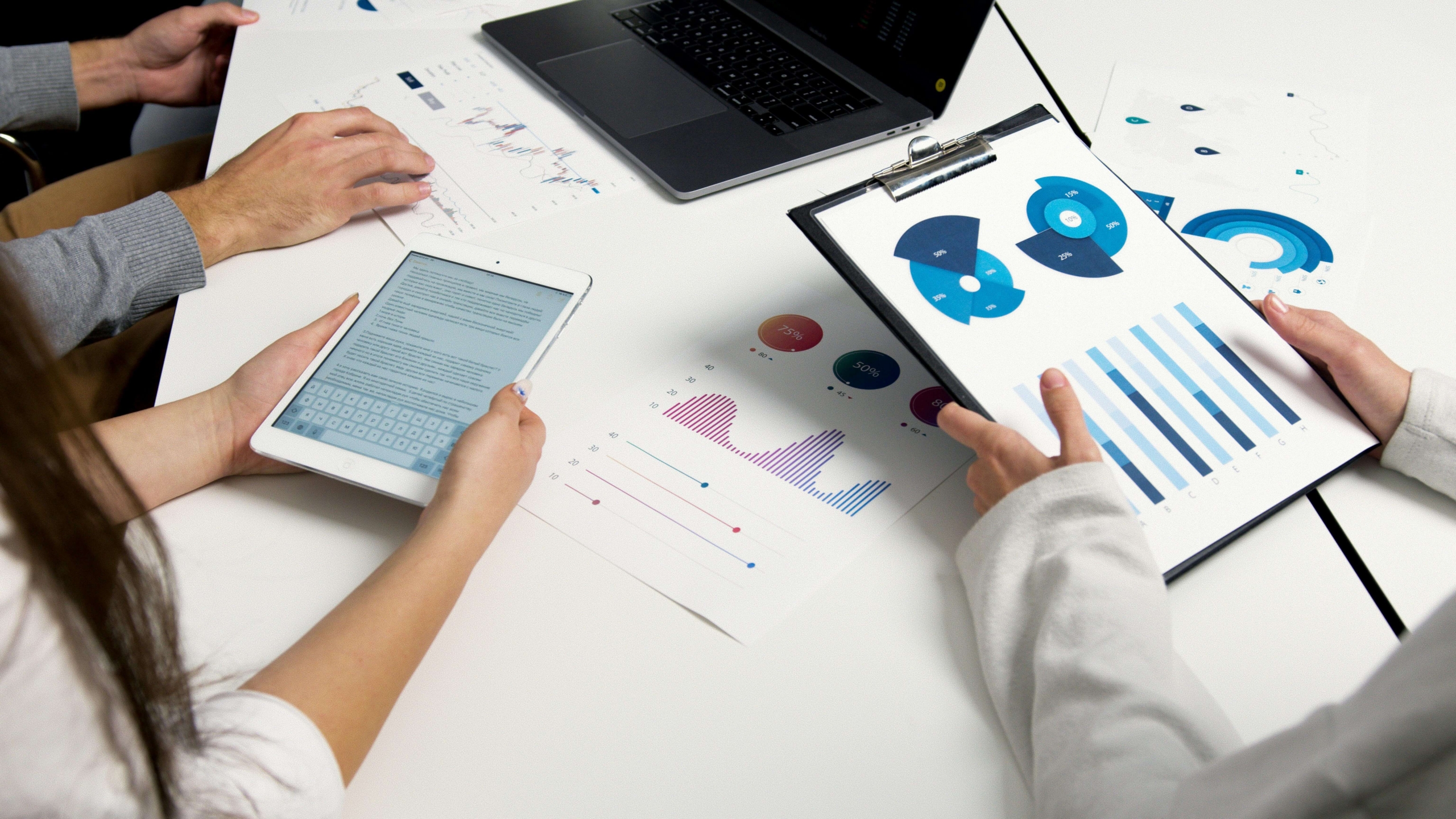 A team of employees hold analytics & data over a table to analyze information.