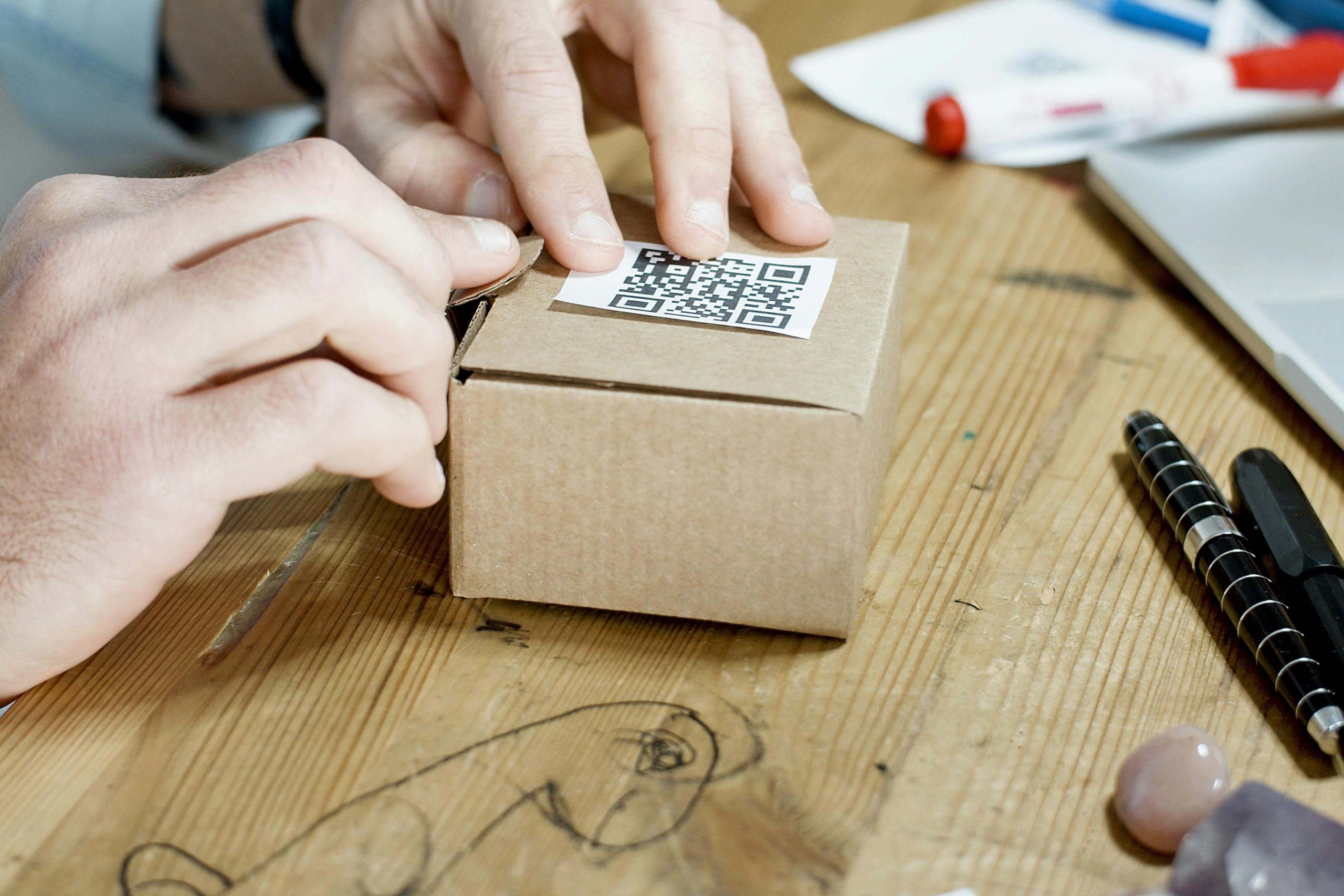 A customer places a QR code onto a product on a work desk with pens and markers.
